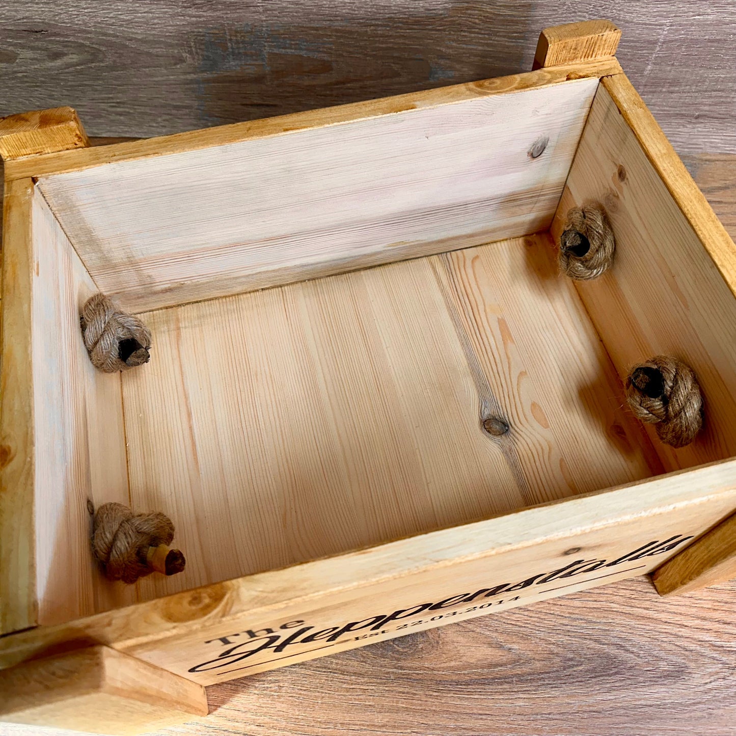 Interior view of a rustic wooden keepsake box showing knotted rope handles securely fixed to the inner sides.
