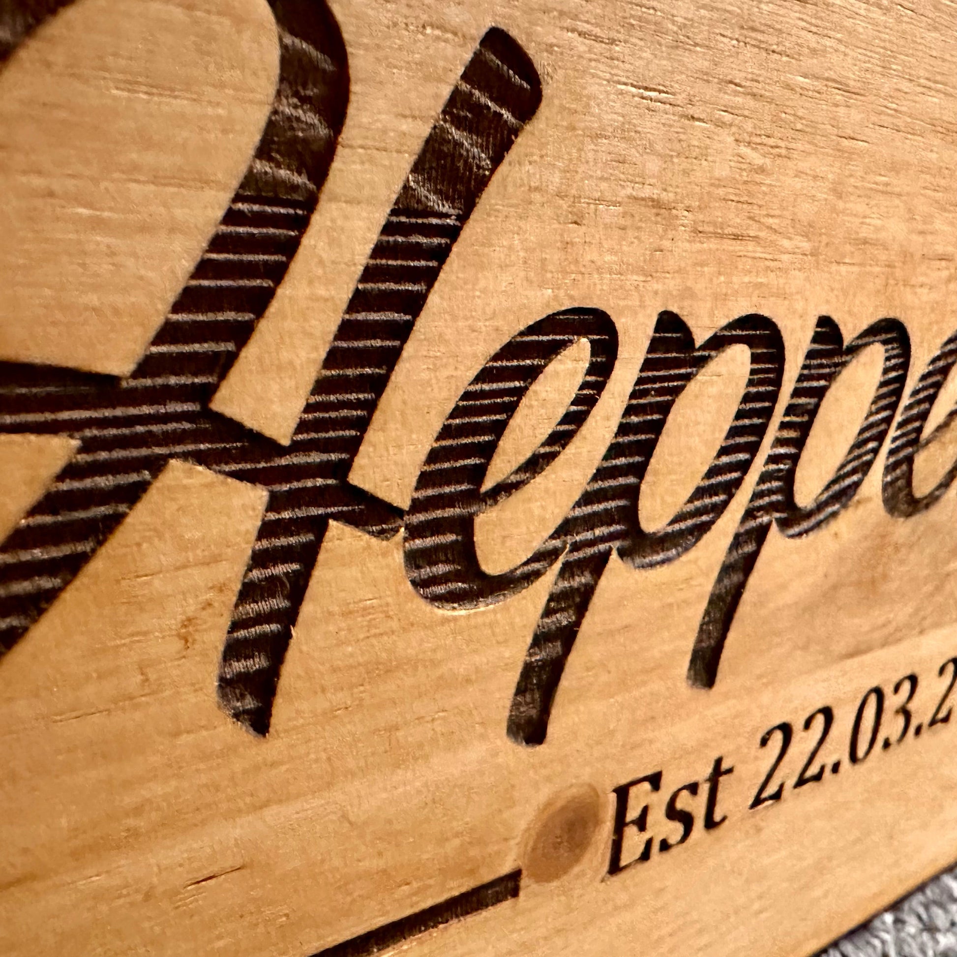 Close-up of detailed engraving on a wooden keepsake box showing the word “Heppenstalls” with visible carving lines and rich wood texture.