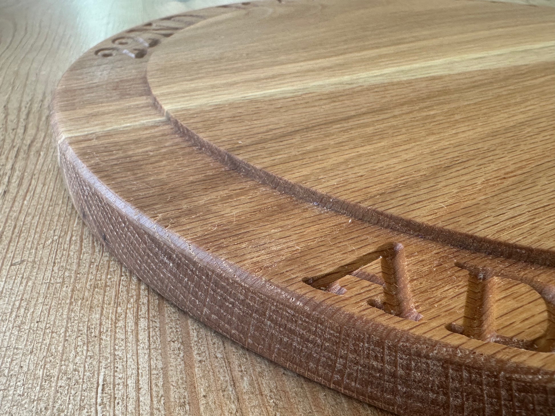 Close-up side detail of a personalised oak cake stand engraved with “ADAM AND LIANNE,” showing crisp carving and rich wood texture.