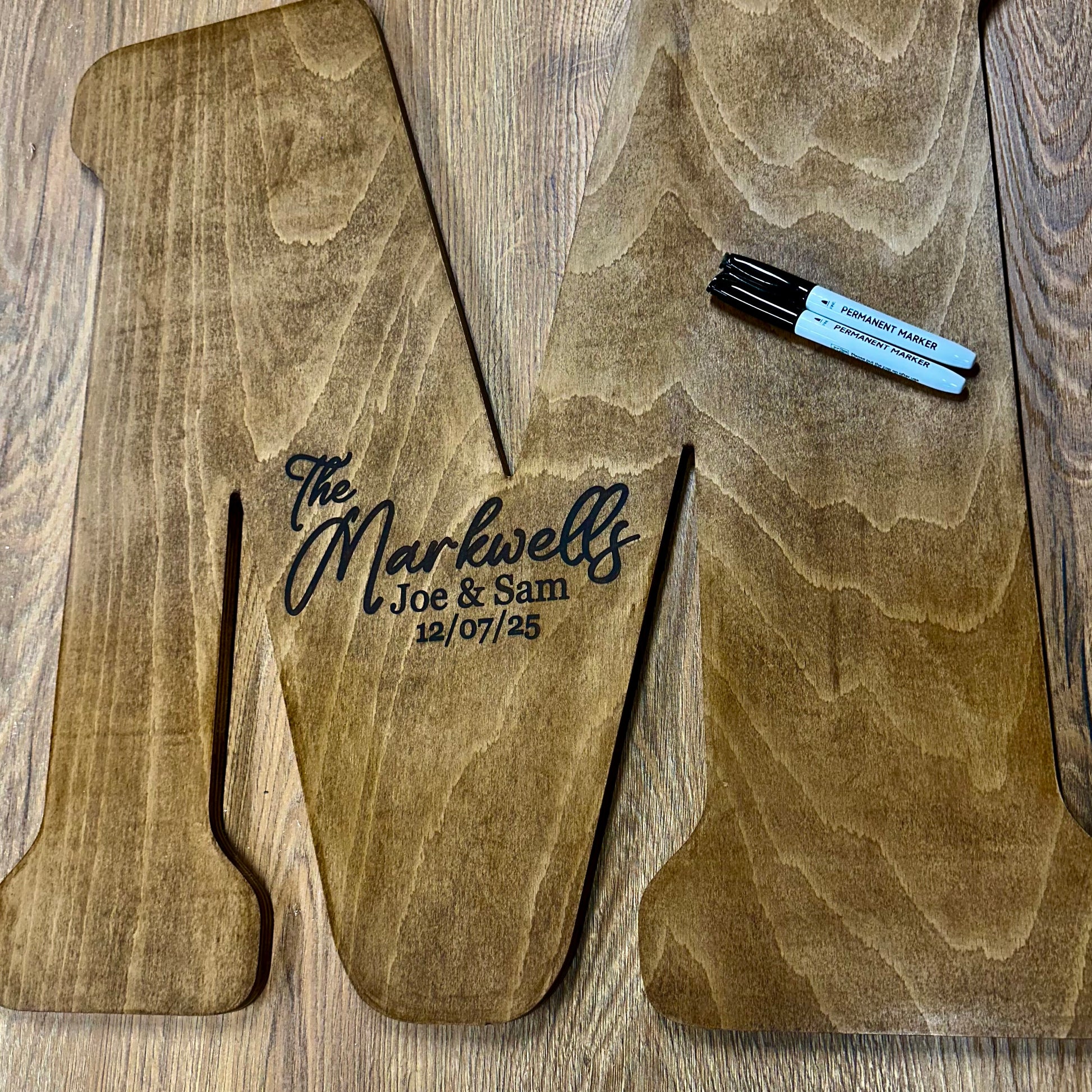 Wooden guestbook letter “M” engraved with “The Markwells – Joe & Sam – 12/07/25” including permanent markers ready for guest messages.