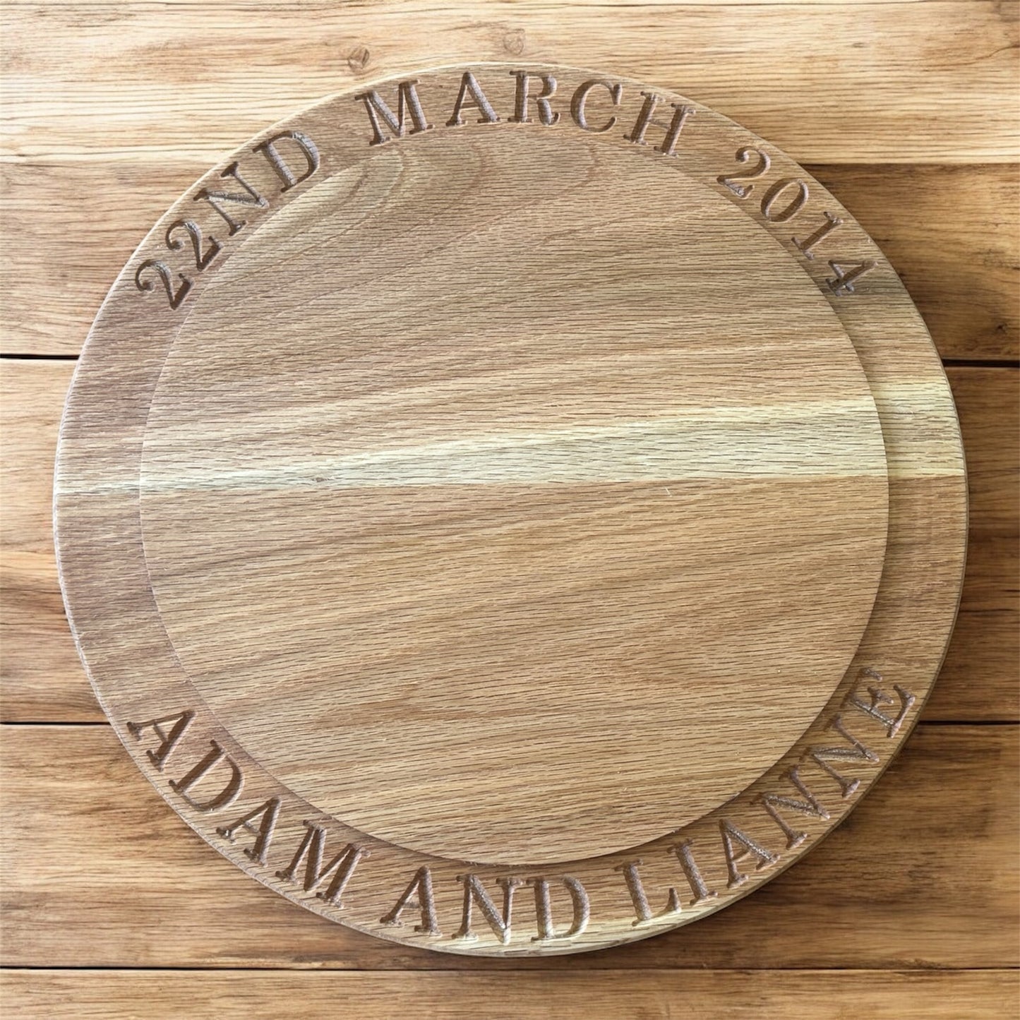 Flat lay of a personalised oak cake stand engraved with “22nd March 2014” and “Adam and Lianne,” showcasing beautiful wood tones and precise carving.