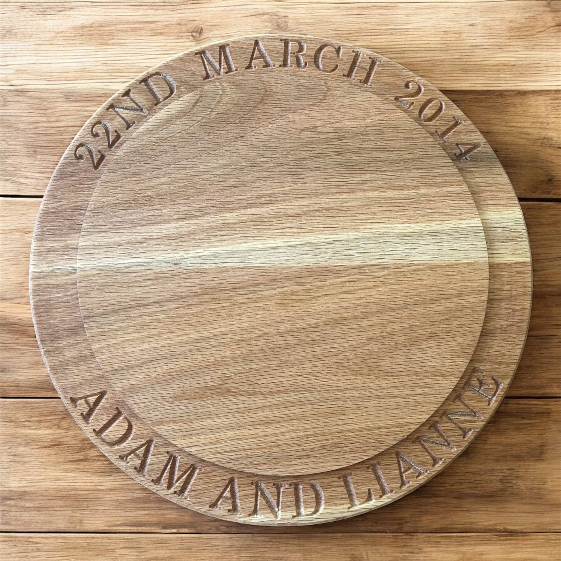 Flat lay of a personalised oak cake stand engraved with “22nd March 2014” and “Adam and Lianne,” showcasing beautiful wood tones and precise carving.
