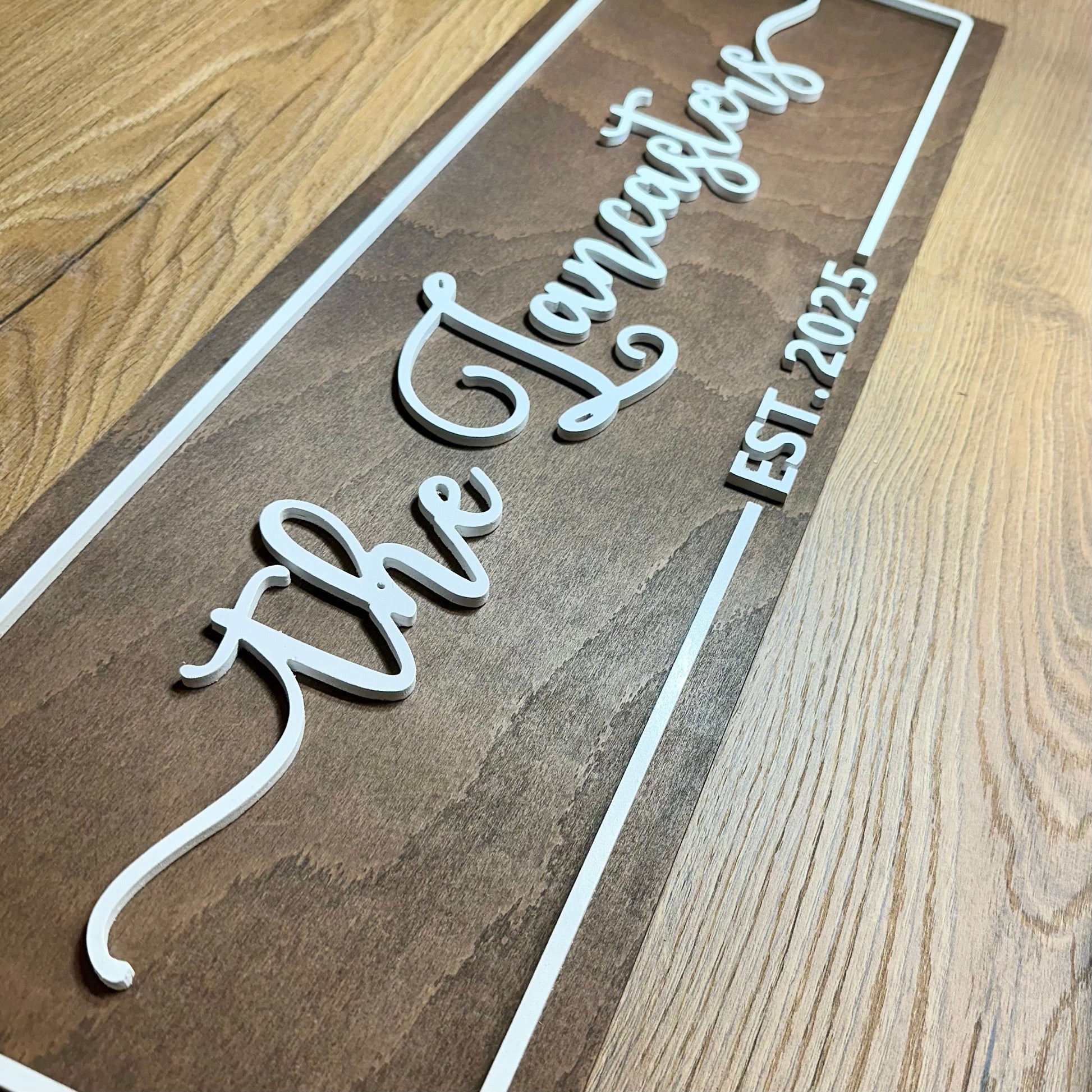 Side view of a handcrafted wooden name sign featuring “The Lancasters – Est. 2025” with raised white lettering and detailed edging.